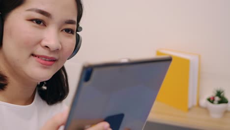 Beautiful-asian-woman-look-camera-and-smile-relaxing-and-listening-to-music-by-tablet-with-headphones-on-the-bed-at-home-lifestyle-and-pleasure-concept
