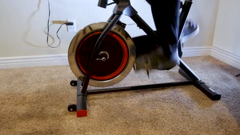 Man's-legs-seen-as-he-pedals-on-a-stationary-bicycle-in-his-home-for-exercise---sliding-close-view