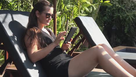 Medium-Side-Shot-of-a-Young-Woman-Reading-an-E--Book-on-a-Tablet-by-the-Pool