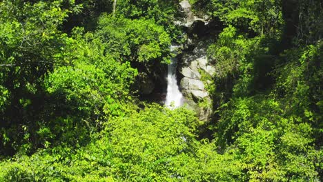 Fresh-white-water-rushing-down-rocky-mountainside-of-Saltos-Jima-waterfall-nestled-in-green-foliage-landscape,-Bonao,-Dominican-Republic,-rising-aerial-tilt-down