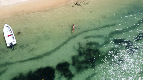 Descend-aerial-drone-shot-of-woman-lying-in-crystal-clear-ocean-on-sunny-day