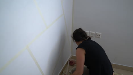 Caucasian-woman-applying-paper-tape-on-wall,-preparing-for-painting-indoors