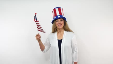 A-senior-woman-waves-a-flag-in-celebration-of-patriotic-feelings-while-wearing-a-hat-with-stars,-and-stripes-of-red-white-and-blue