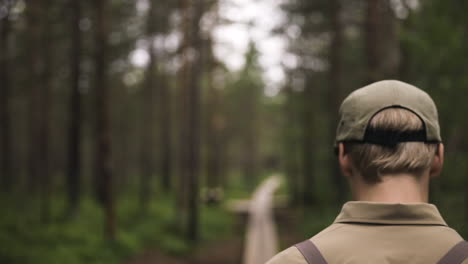 Close-follow-shot-of-young-man-with-cap-walking-through-green-forest