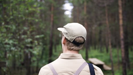 Close-view-from-behind-of-blonde-man-with-cap-walking-through-forest