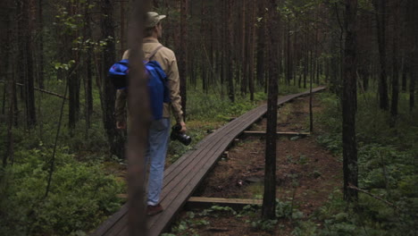 Male-photographer-walks-on-wooden-pathway-through-forest,-slow-pan