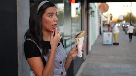 A-cute-young-hispanic-woman-licking-an-ice-cream-cone-and-smiling-with-happiness-at-a-dessert-shop-on-a-city-street-SLOW-MOTION