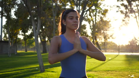 A-pretty-hispanic-woman-in-a-prayer-hands-yoga-pose-meditating-in-the-park-at-sunrise