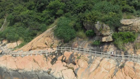 Zoom-out-aerial-reveal-shot-of-man-with-backpack-walking-along-rocky-coastal-trail