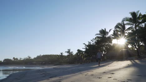 Man-enjoying-a-stroll-on-tropical-white-beach-in-Fiji-during-sunrise,-static