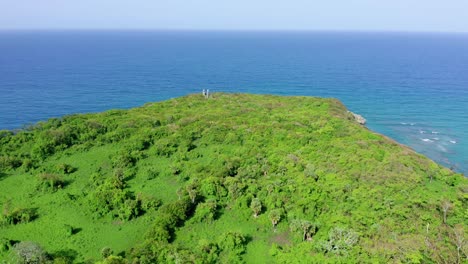 A-Spectacular-Green-Grass-Covered-Cliff-in-front-of-Calm-Beautiful-Blue-Atlantic-Ocean,-Circle-Orbit-Drone-Shot,-Dominican-Republic