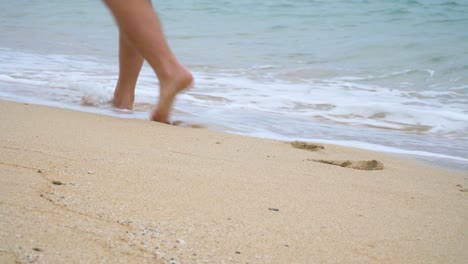 Close-up-of-mans-feet-walking-on-sandy-beach-next-to-water,-stroll-in-paradise