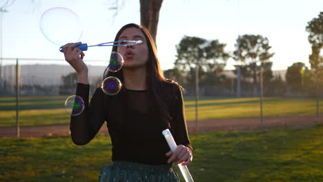 Gorgeous-hispanic-woman-blowing-dreamy-bubbles-while-smiling-and-looking-playful-outdoors-at-sunset