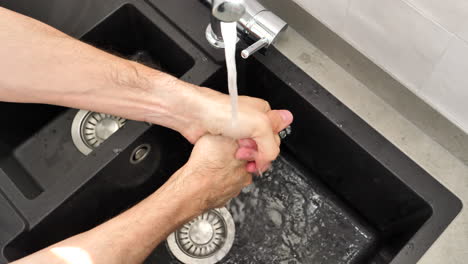 Man-washing-hands-in-kitchen-sink