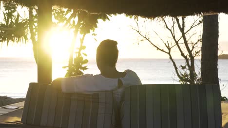 Woman-enjoying-beautiful-Fijian-sunset-at-resort-cabana,-behind-view,-dolly-out