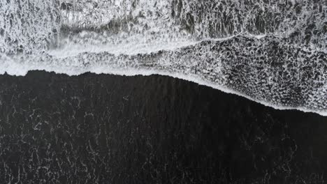 Top-down-drone-shot,-waves-rush-up-black-sand-beach-shore