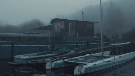 Barge-houseboat-moored-along-shoreline-among-dense-atmospheric-fog