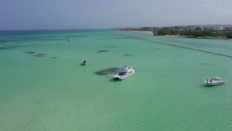 Die-Epische-Drohnenkreisbahn-Einer-Superyacht-Und-Drei-Motorboote-Liegen-Vor-Anker-Im-Klaren,-Blaugrünen-Wasser-Von-Playa-Juanillo,-Dominikanische-Republik