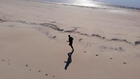Aerial,-drone-shot-following-a-man-running-on-a-beach,-sunny-day,-on-Langeoog-island,-at-the-Nordsee,-in-North-Germany
