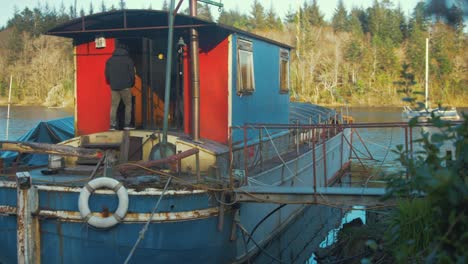 Young-man-living-on-Barge-houseboat-carrying-logs-enters-wheelhouse