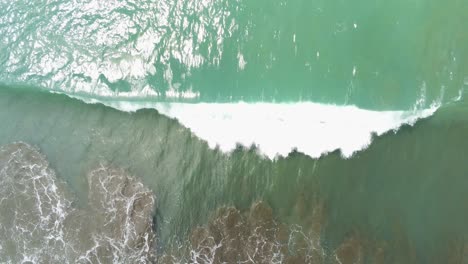 Top-down-aerial-drone-view,-lone-wave-crashes-into-white-foam