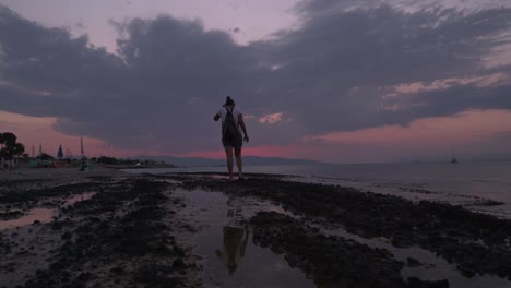 Weitwinkelaufnahme-Einer-Kaukasischen-Frau,-Die-Am-Späten-Abend-Am-Strand-Spazieren-Geht,-Mit-Wunderschönem-Sonnenuntergang-Im-Hintergrund-4k