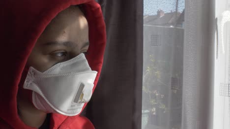 Red-Hooded-Female-Child-Wearing-FFP-Three-Mask-Indoors-Looking-Through-Curtains-Contemplatively