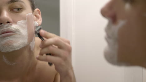 A-man-shaving-his-beard-using-a-razor-and-some-shaving-cream---close-up