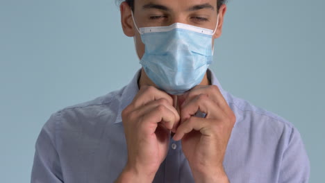 Ein-Professionell-Aussehender-Mann,-Der-Seine-Chirurgische-Gesichtsmaske-Trägt,-Die-Richtig-Auf-Blauem-Hintergrund-Steht---Ausbruch-Des-Coronavirus---Nahaufnahme