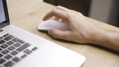 Close-shot-of-young-male-hand-using-white-mouse-beside-laptop-on-table