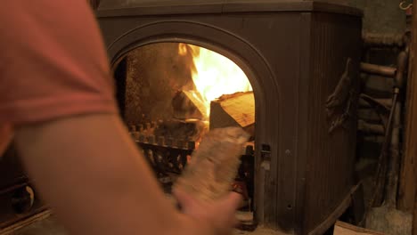 Young-man-loading-up-stove-with-birch-logs-stokes-embers-closes-door