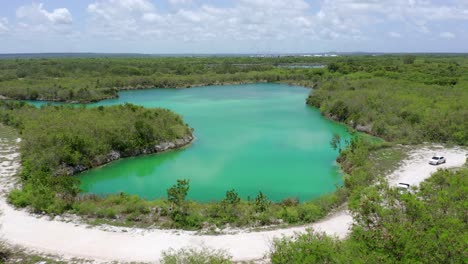 Low-altitude-flight-overlooking-blue-lake-in-cap-cana,-turquoise-blue-waters,-two-white-vans-passed-on-a-warm-day