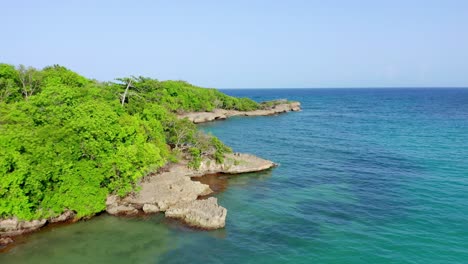 Drohne-Fliegt-über-Klares-Tropisches-Wasser-Und-Eine-Prächtige-Felsige-Baumbewachsene-Küstenlinie-Am-Strand-Von-Playa-Diamante-In-Der-Dominikanischen-Republik