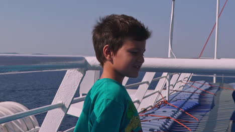 Caucasian-greek-boy,-enjoying-the-trip,-at-the-deck-of-ferry-boat,-strong-wind-blows-his-hair-120fps