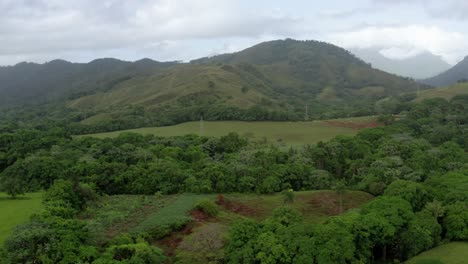 Slow-aerial-shot-at-low-altitude,-green-fields,-clouds,-fresh-breeze-in-Bonao,-Dominican-Republic