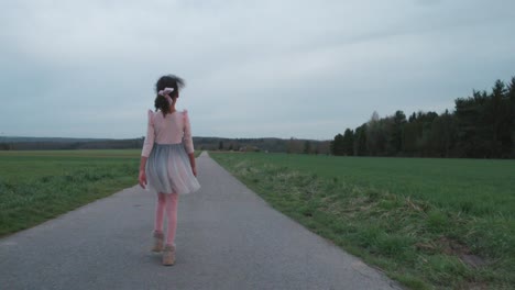 Little-girl-in-ballerina-dress-walking-happily-down-field-road