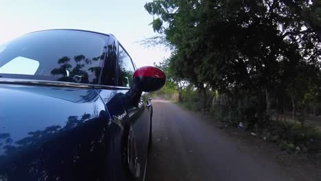 hatchback-car-running-at-high-speed-among-tropical-forest,-dusty-road