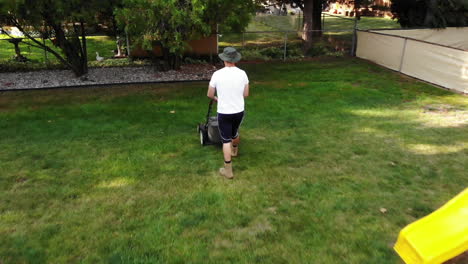 A-low-aerial-rear-view-of-a-man-mowing-his-backyard-lawn