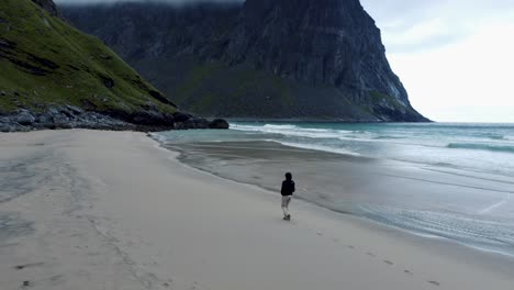 Flying-at-a-beach-in-Norway,-focused-is-a-person-walking-along-the-water-on-an-empty-beach-