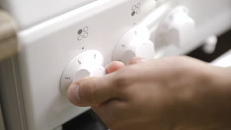 Male-hand-turns-on-stove-to-full-heat-using-control-wheel,-close-up