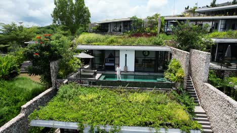 Luftdrohne-Eines-Jungen-Kaukasischen-Models,-Das-An-Einem-Sonnigen-Sommertag-In-Bali,-Indonesien,-Vor-Einem-Beliebigen-Infinity-Pool-In-Einer-Privaten-Weißen-Luxusvilla-In-Einem-Hotel-Und-Resort-Spazieren-Geht