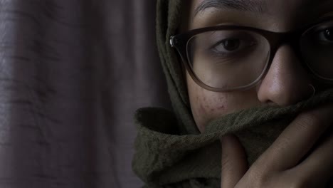 Woman-Wearing-Glasses-Holding-Hijab-Covering-Her-Mouth-Looking-At-Camera