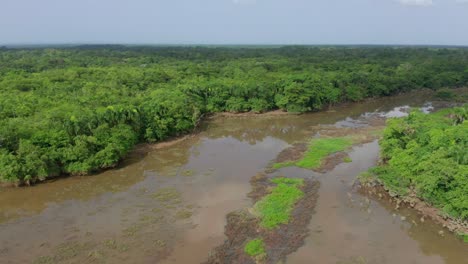 Scenic-shot-with-drone-of-the-Ozama-river-in-the-place-where-it-is-born,-brown-cloudy-waters,-green-vegetation-on-a-cloudy-day,-tropical-jungle-environment