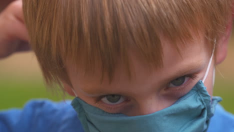 Der-Kleine-Junge-Zieht-Eine-Stoffmaske-An,-Um-Sich-Vor-Der-Coronavirus-Krankheit-Zu-Schützen