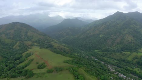 Aerial-shot-between-mountains-in-Bonao-Dominican-Republic,-rain-clouds,-town-in-the-background