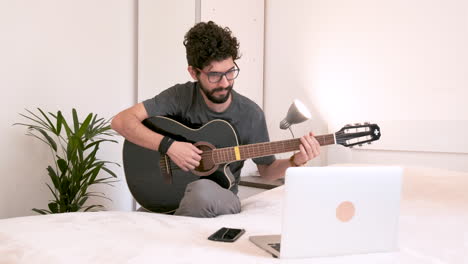 Man-playing-guitar-in-the-room-in-front-of-laptop-on-light-background,-isolated