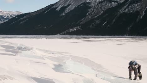 Niña-Excursionista-Deslizándose-Por-Una-Losa-De-Hielo-Gigante-En-Hermosas-Montañas-De-Invierno-En-El-Lago-Congelado-Minnewanka-En-El-Parque-Nacional-De-Banff-Alberta-Canadá-En-Un-Día-Soleado-Al-Aire-Libre