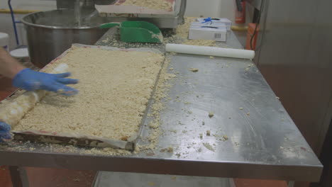 Ein-Arbeiter-An-Einem-Edelstahlarbeitsplatz-Bereitet-Kuchenmischung-Auf-Einem-Großen-Tablett-Zu,-Das-Dann-Für-Den-Ofen-Bereit-Gestellt-Wird