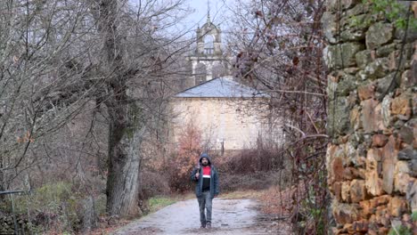 Young-man-walks-out-of-a-rural-church-in-the-middle-of-the-nature-after-a-rainy-day-with-a-close-umbrella-on-his-hand
