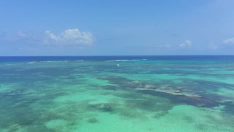 Sensational-scenic-flight-above-turquoise-ocean-sea-towards-single-anchored-motor-boat-in-water-on-sunny-day,-Cap-Cana,-Dominican-Republic,-overhead-aerial-approach